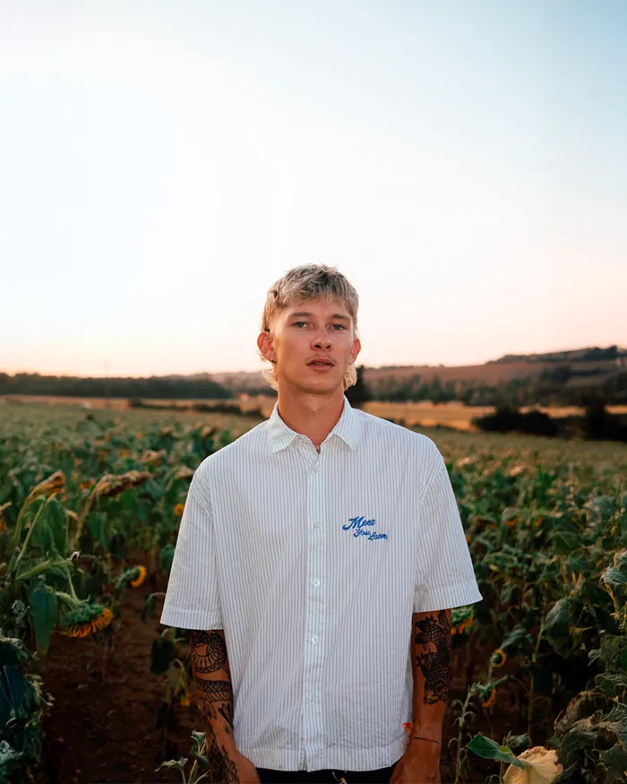 Portrait de Guénolé Savary face à l'objectif, debout dans un champ de tournesols au crépuscule.